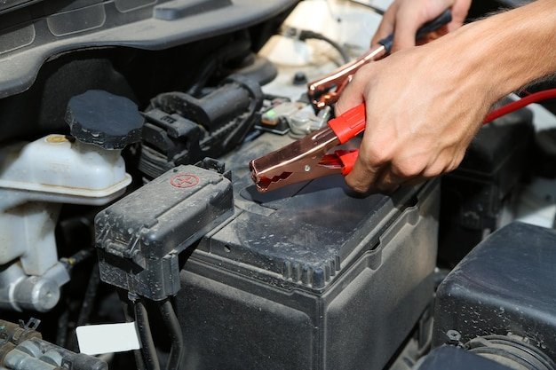 Car mechanic uses battery jumper cables to charge dead battery