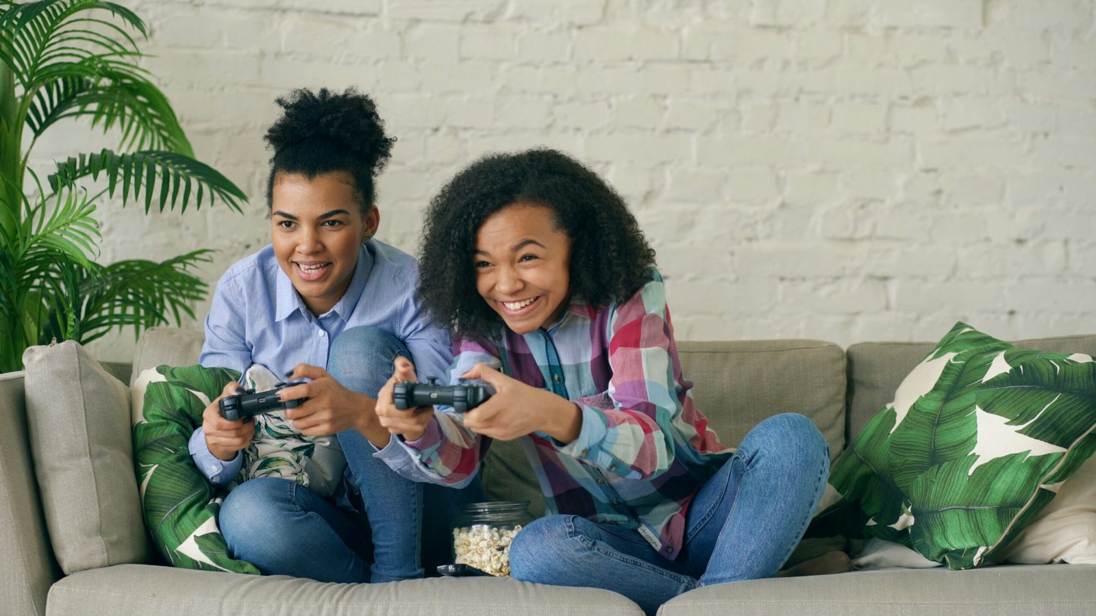 Two smiling girls playing video games on couch.