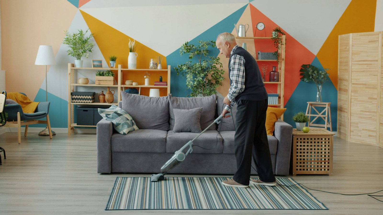 Elderly woman vacuuming a colorful living room floor.