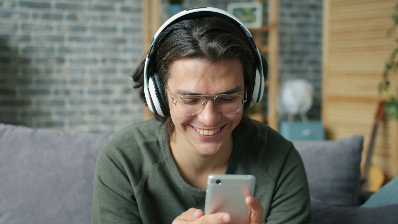 Young man wearing headphones smiles at phone.
