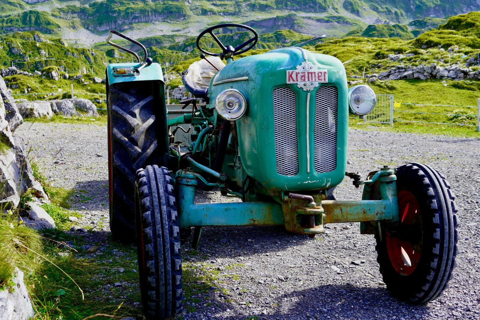 an old green tractor parked on a gravel road