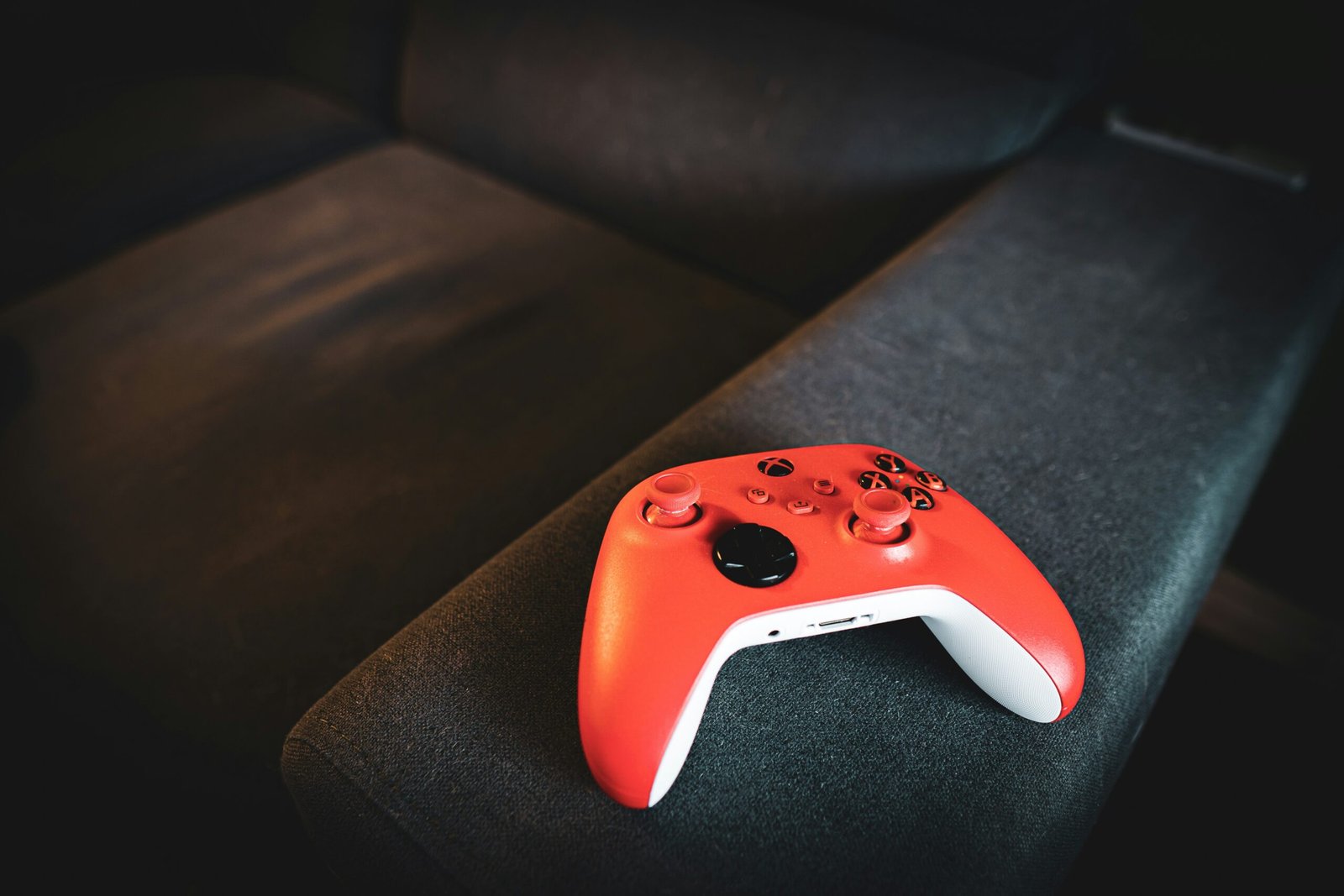 Red video game controller rests on a dark couch