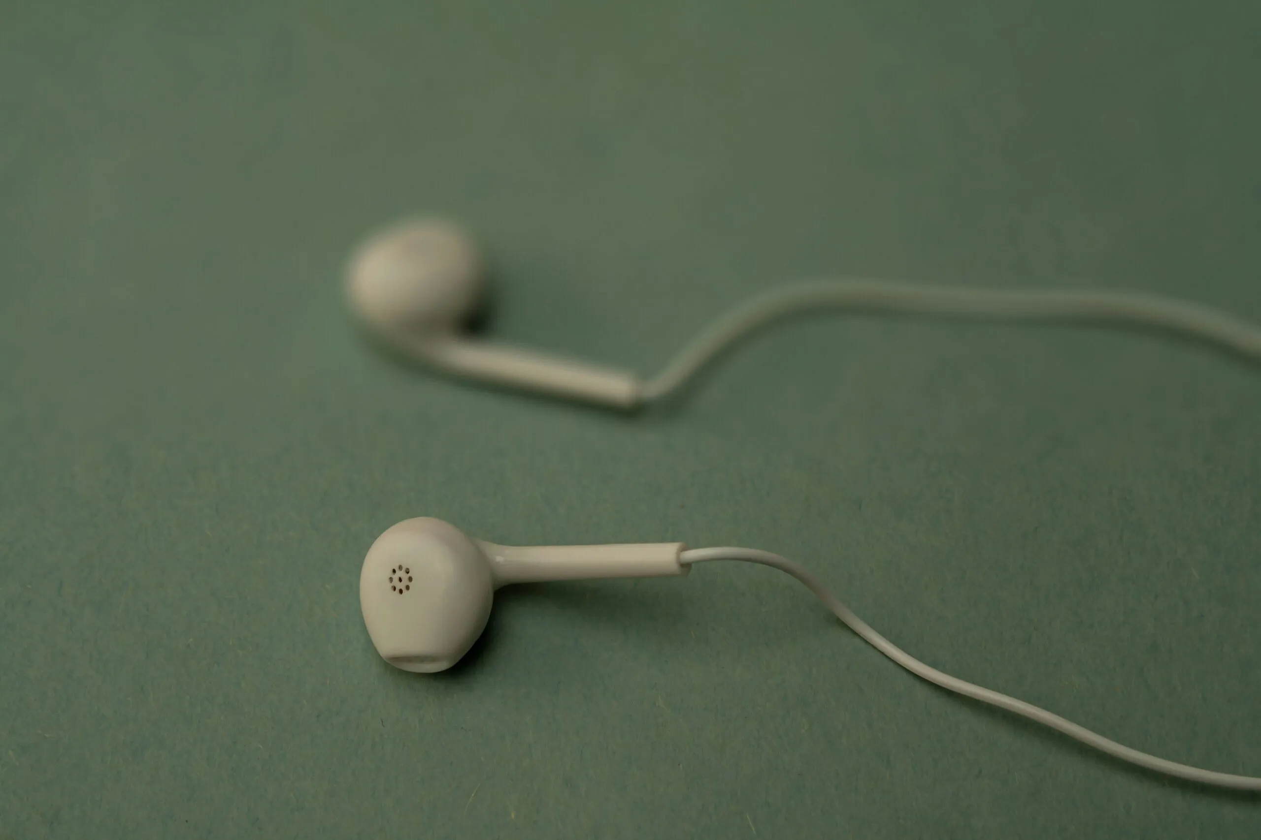 White earbuds lie on a teal background.