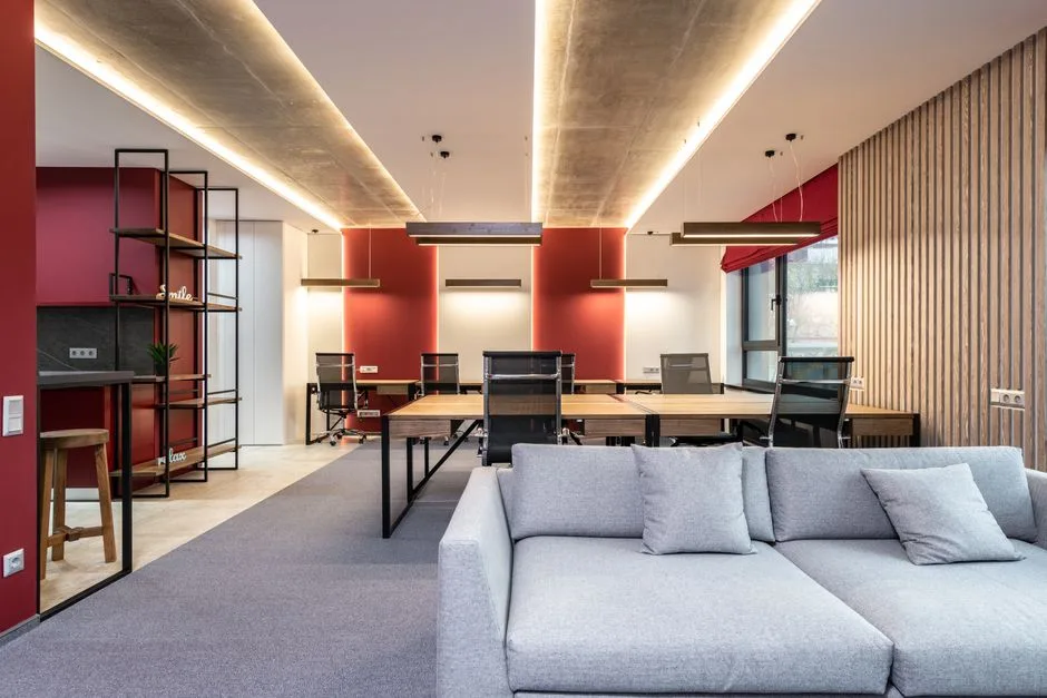 Interior of modern office lounge zone with sofa with pillows near tables with chairs next to shelves and windows