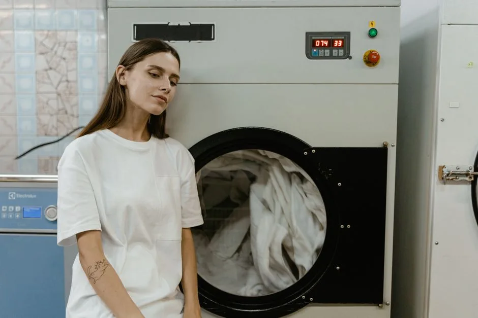 A woman in a laundry facility standing by a washing machine, contemplating the process.