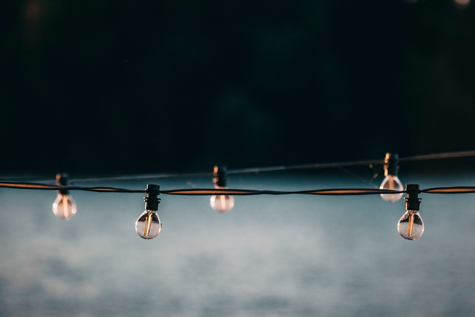 Small switched off electric lamps on long wire strained above gray blurred surface