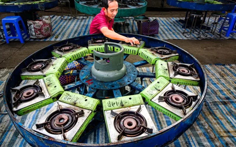 A man arranges stove burners around a central gas cylinder outdoors.