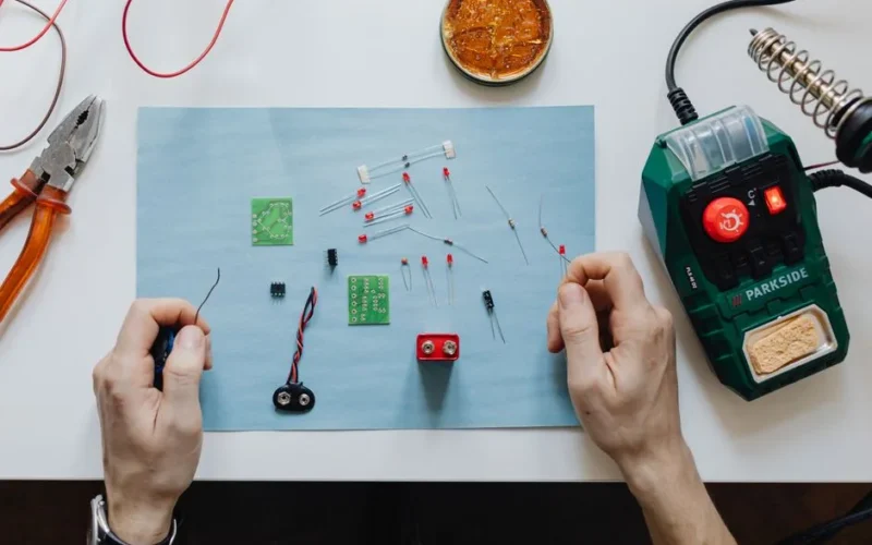 Hands-on electronics repair with tools, circuit board, and soldering station on workspace.