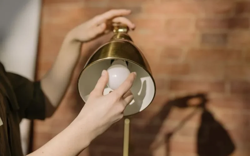 Hands changing a light bulb in a lamp with a brick wall background.