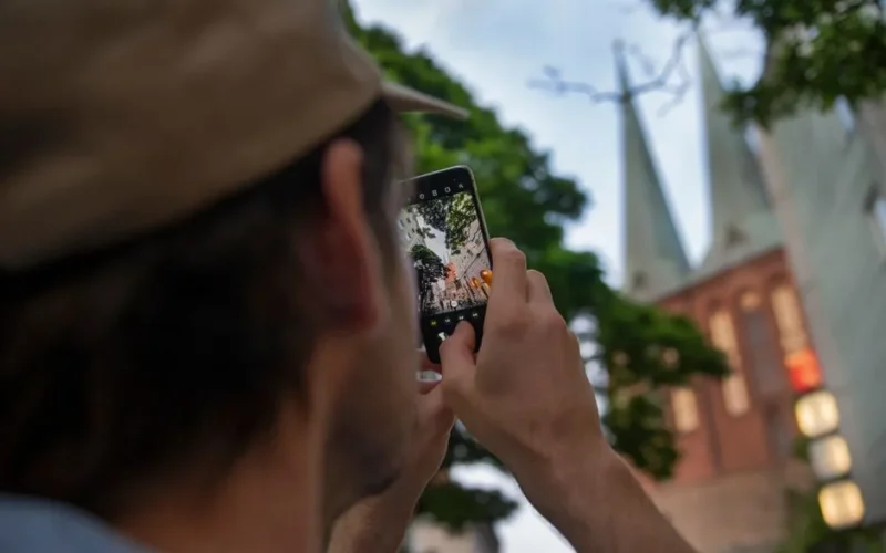 A person captures iconic Berlin church towers using a smartphone, outdoors.