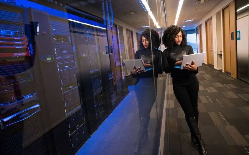A woman using a laptop navigating a contemporary data center with mirrored servers.