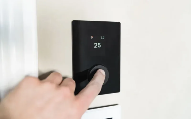 Close-up of a hand adjusting a sleek, modern smart thermostat on a wall.