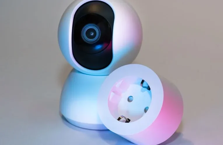 Smart home security camera and plug socket on a neutral background.