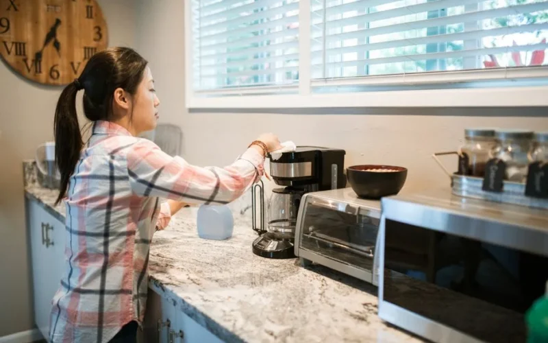 Woman cleaning a coffee maker in a bright, modern kitchen with appliances.