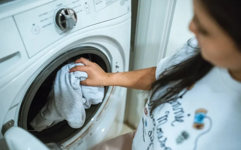 A woman loading laundry into a washing machine indoors, focusing on household chores.