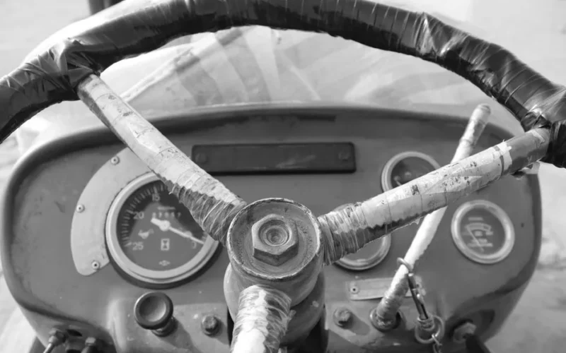 Close-up of a vintage tractor's steering wheel and dashboard in black and white.