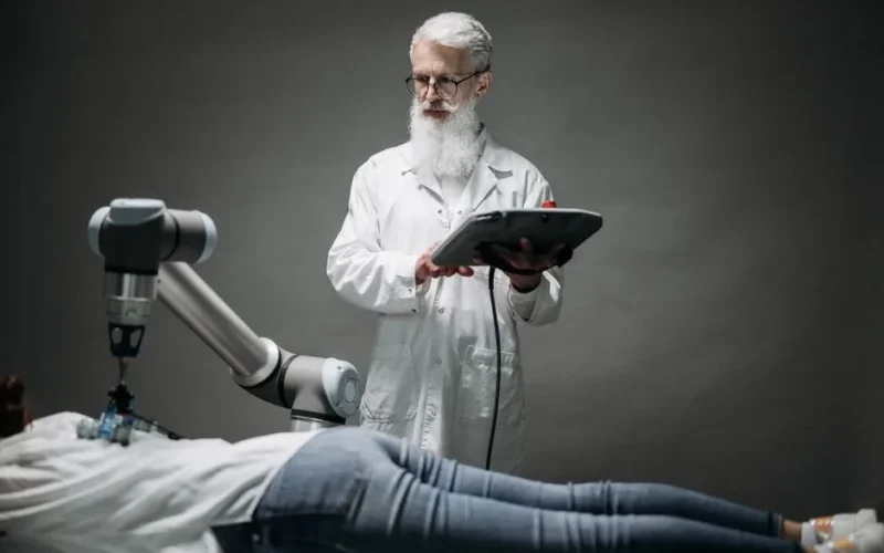 A scientist controls a robotic arm conducting research on a person lying down.