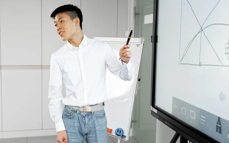 Asian man presenting with smart board in a modern office setting.