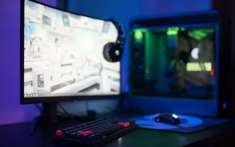 High-tech gaming setup featuring a curved monitor, RGB keyboard, and vibrant lighting.
