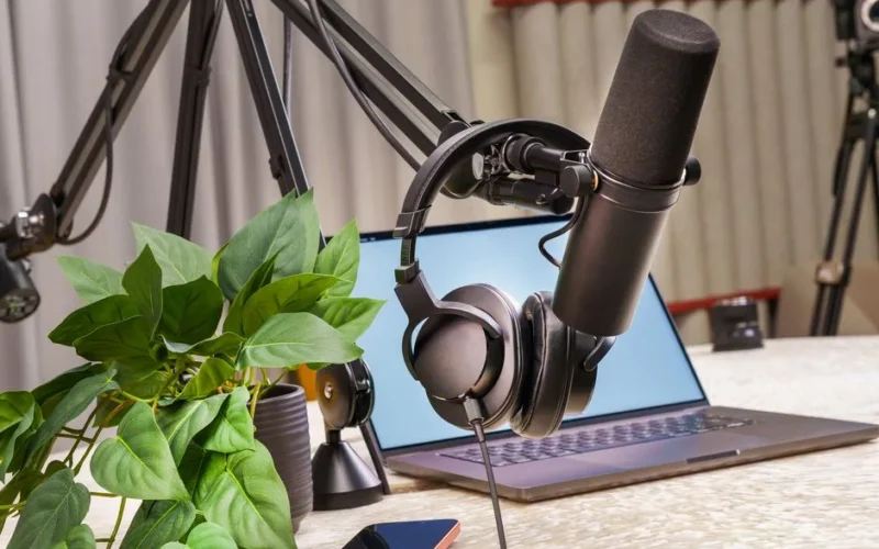 A modern podcast studio setup with a microphone, headphones, and laptop, ideal for media production and online broadcasting.