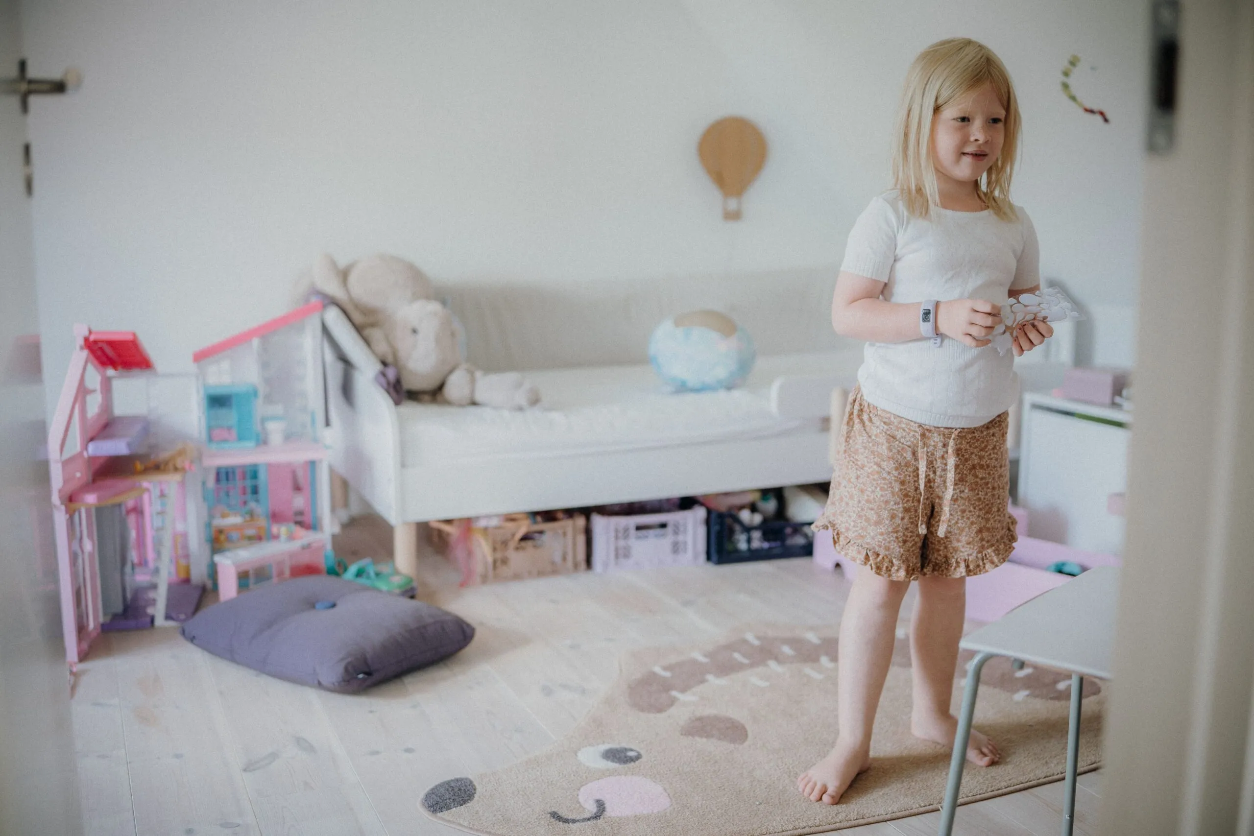 Young girl with blond hair playing in a toy-filled bedroom, creating an endearing childhood moment.