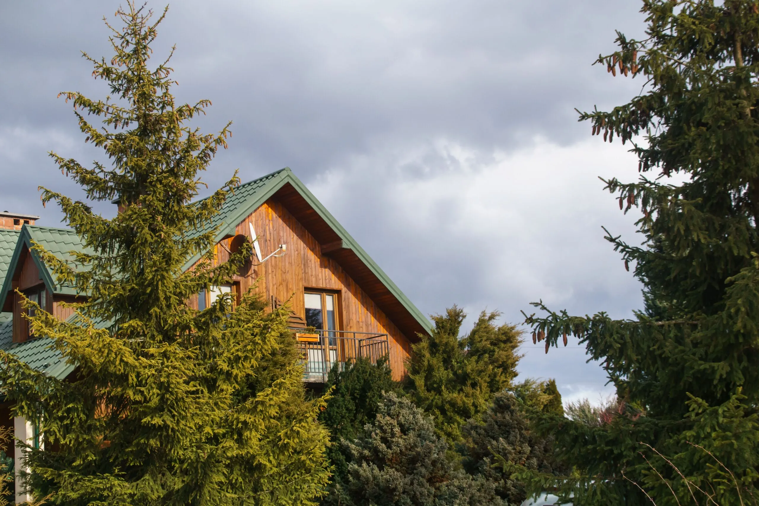 Charming wooden house amidst lush evergreen trees under a cloudy sky.