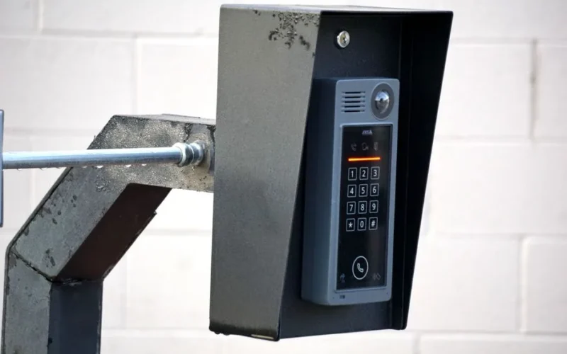 Close-up of a modern security intercom and keypad mounted on a wall outdoors with visible wiring.