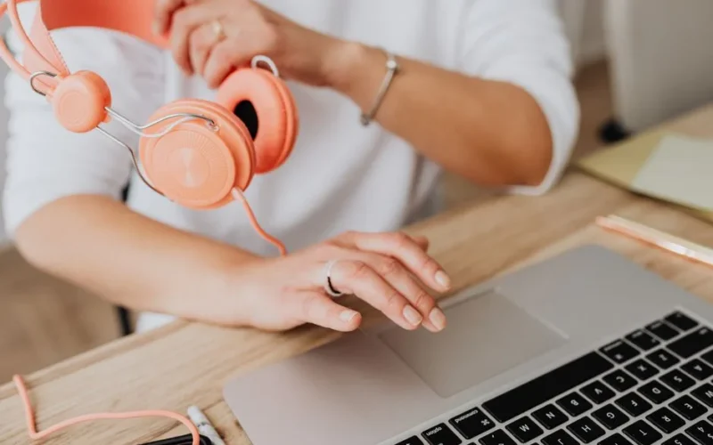 Person holding headphones while using laptop, close-up view.