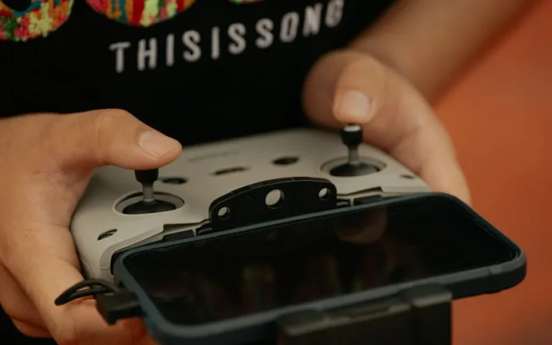 Hands holding a drone controller with a connected mobile device, showcasing modern technology.