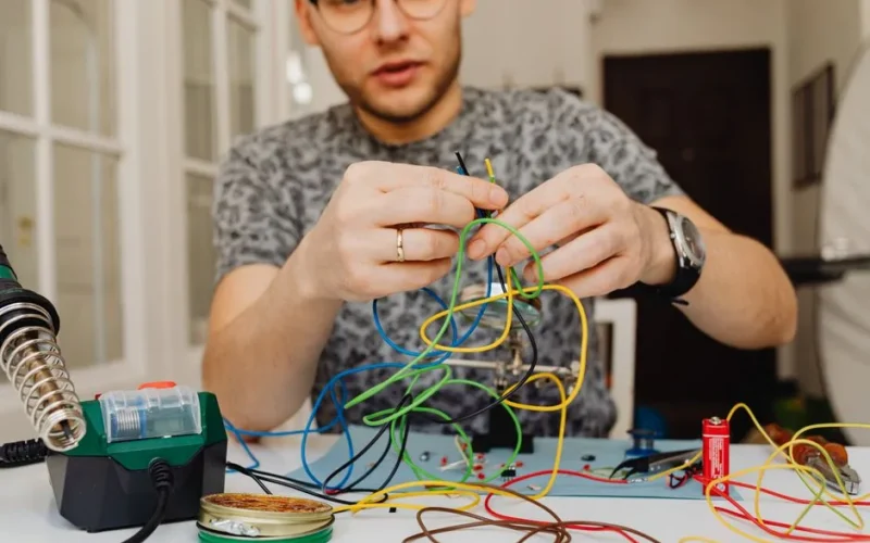 Caucasian man organizing colorful wires indoors with focus on electronics.