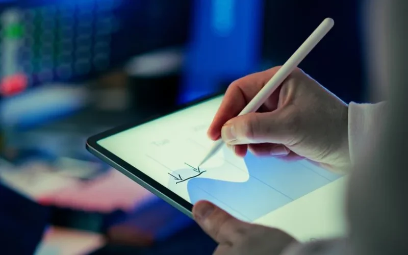 Business person using a stylus to analyze data on a digital tablet in an office setting.