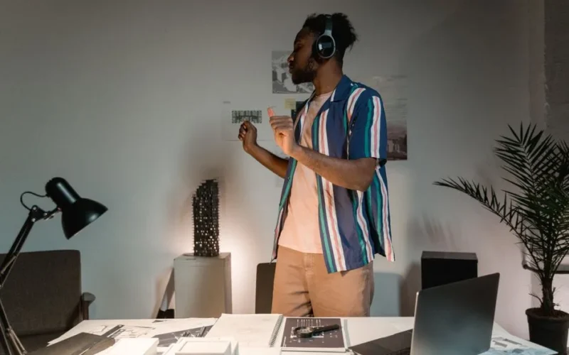 African American man dancing with wireless headphones in a modern home office setting.