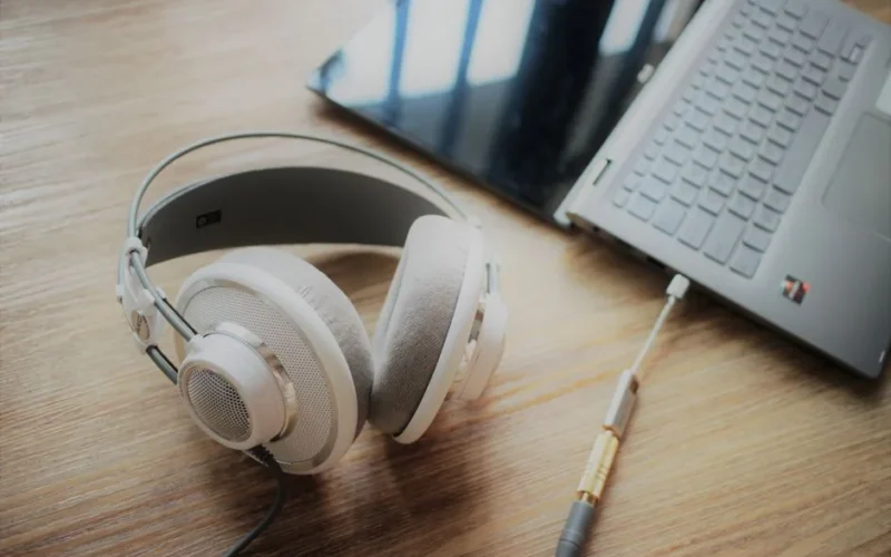Close-up of elegant over-ear headphones connected to a sleek laptop on wooden surface, highlighting modern technology.