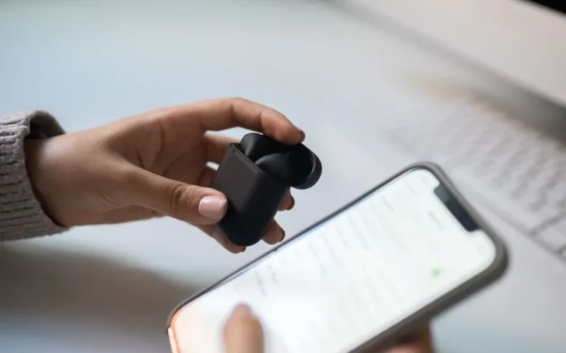 Close-up view of hands connecting wireless earbuds to a smartphone, emphasizing modern technology.