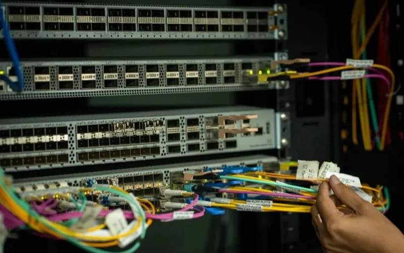 A hand managing fiber optic cables in a server room, showcasing modern connectivity.