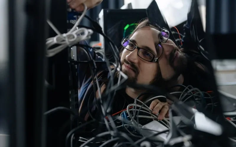 A skilled IT technician organizing tangled cables at his workstation in an office environment.
