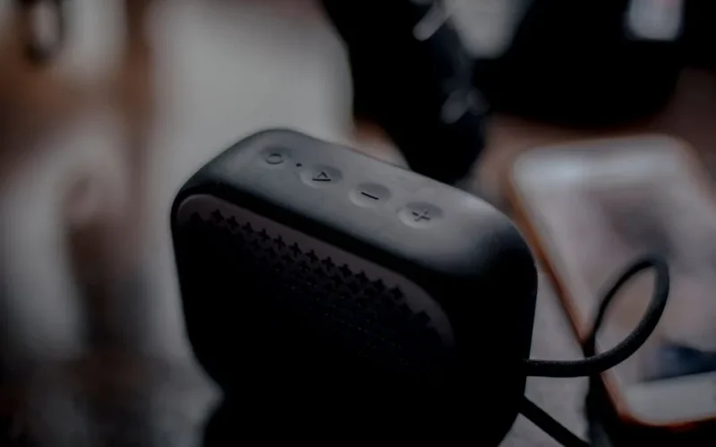 A sleek portable Bluetooth speaker next to a smartphone on a wooden table, emphasizing modern technology.