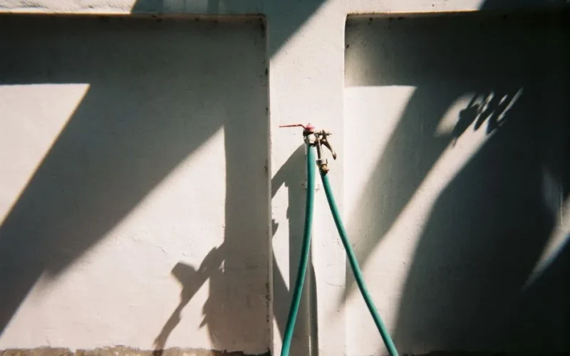 Water tap with hose casting distinct shadows on a wall in daylight.