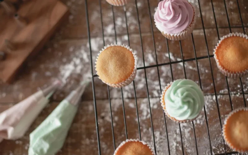 Top view of colorful frosted cupcakes on a cooling rack with piping bags and flour dust.