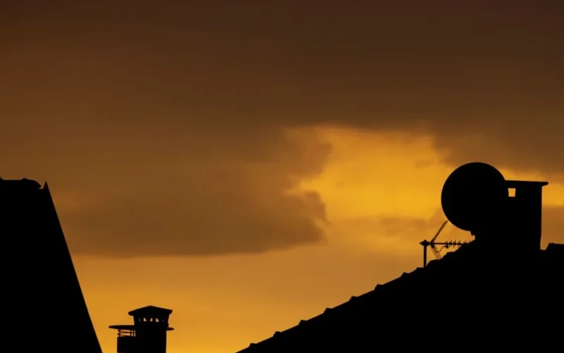 Dramatic silhouette of rooftops and antennas against a vivid sunset sky.
