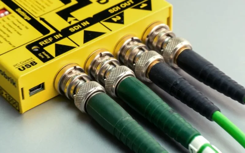 Vibrant close-up of green SDI cables connected to yellow device with visible USB port.