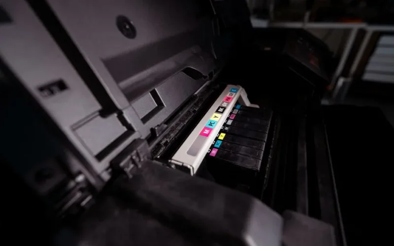 Detailed view of open printer with visible CMYK ink cartridges in a dark setting.