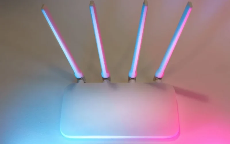 Sleek white wireless router with four antennas emitting soft blue and pink light.
