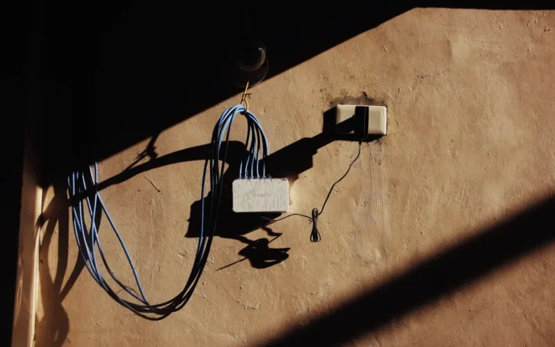 Electric blue wires connected to network adapter plugged in socket on shabby brown wall of building on street with shadow