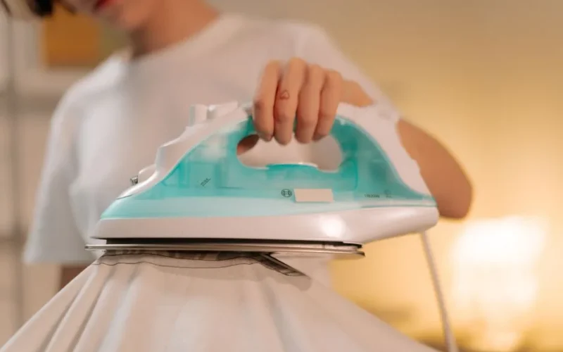Close-up of a person using a steam iron for smoothing a white garment indoors.
