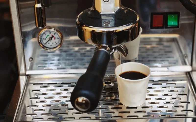 Close-up of an espresso machine brewing coffee into a paper cup.
