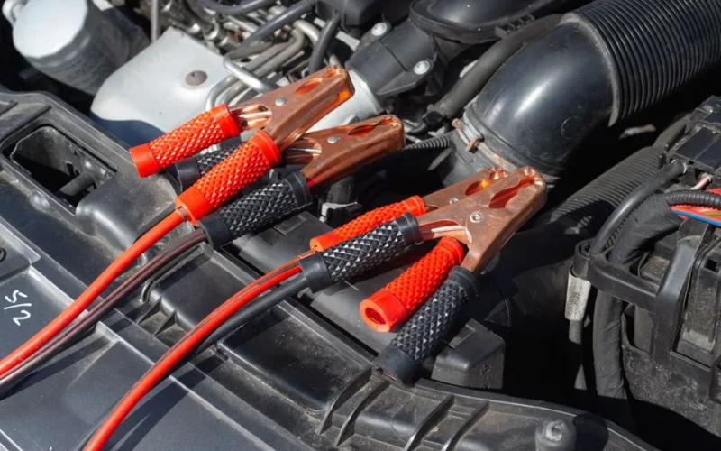 Close-up of car engine with attached jump starter cables, showing detailed mechanics.