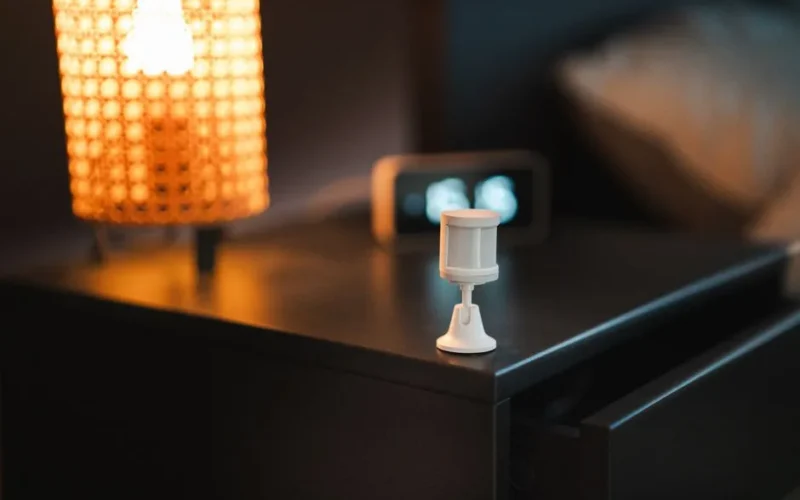 Stylish bedroom with smart motion sensor, lamp, and alarm clock on wooden nightstand.