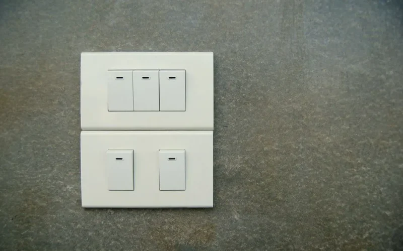 Minimalist photo of white electrical rocker switches on a textured stone wall background.