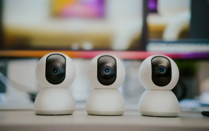 Three modern smart home security cameras placed on a table indoors with a blurry background.